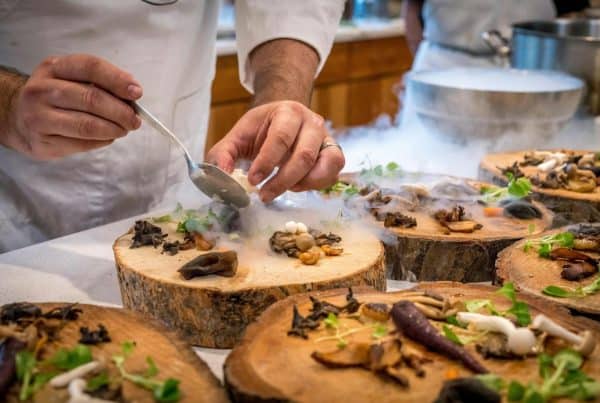 A chef artfully plating a gourmet dish with mushrooms and greens on wood slices.