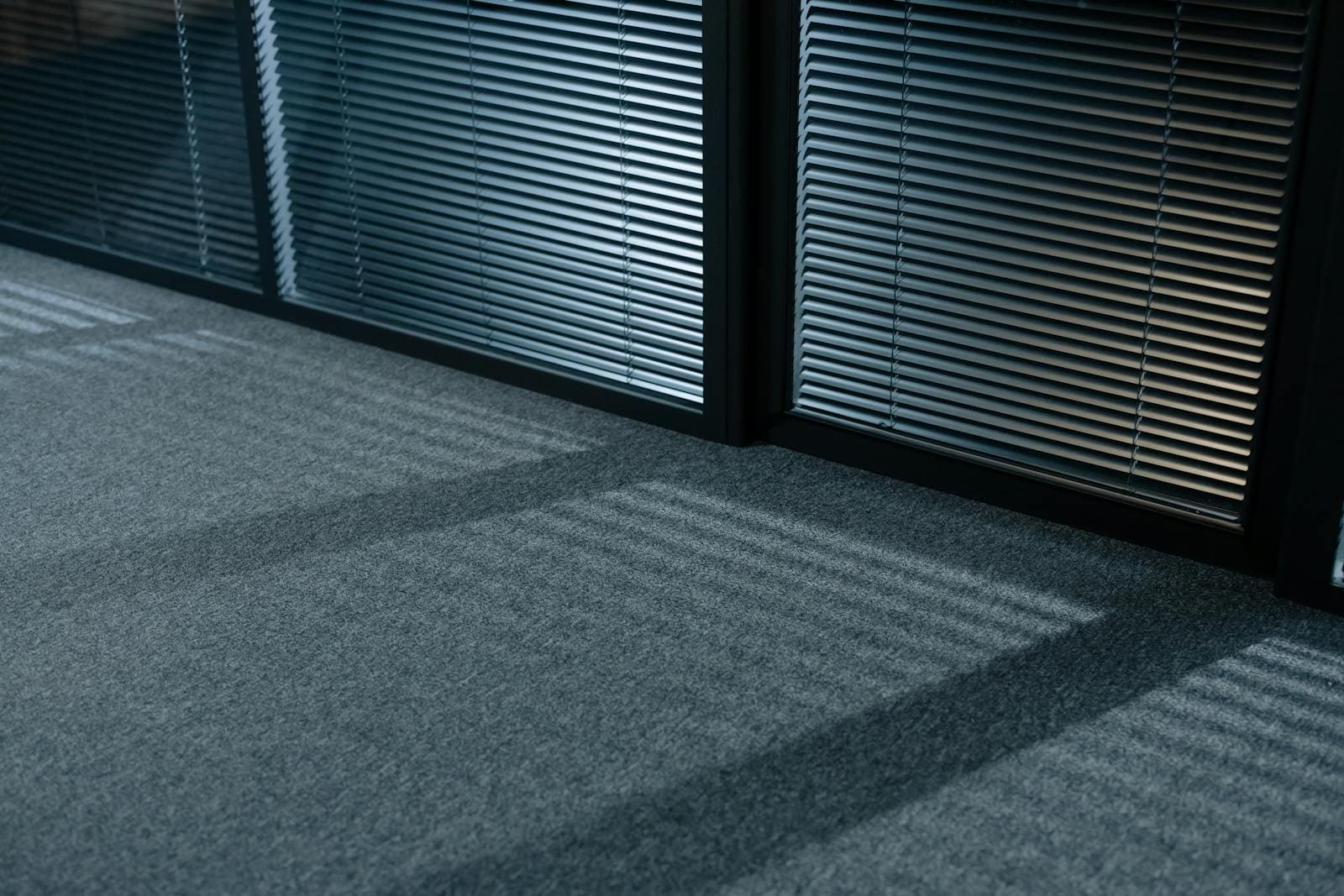 A serene indoor space with shadows and venetian blinds casting lines on a carpeted floor.